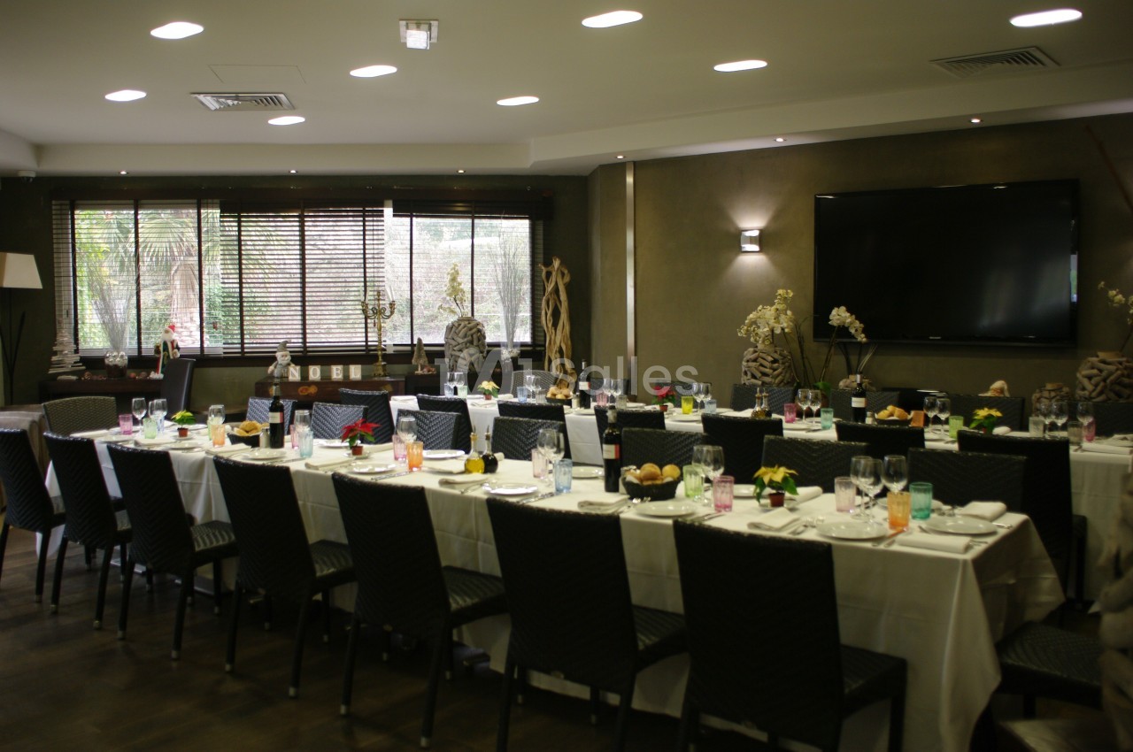 Salle de réception avec de longues tables dressées, chaises noires, décoration élégante et grande télévision murale.