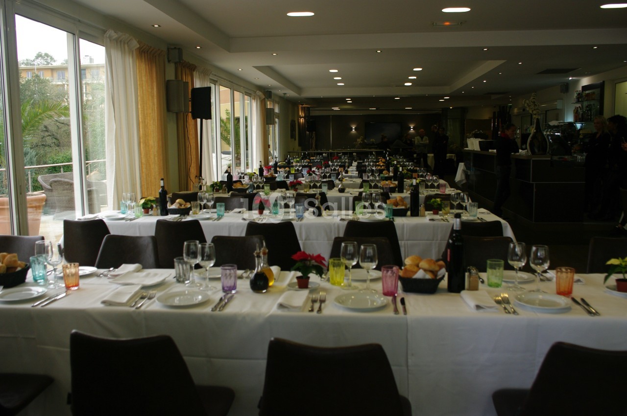 Salle de réception avec tables dressées, nappes blanches, verres colorés et couverts, prête pour un événement.