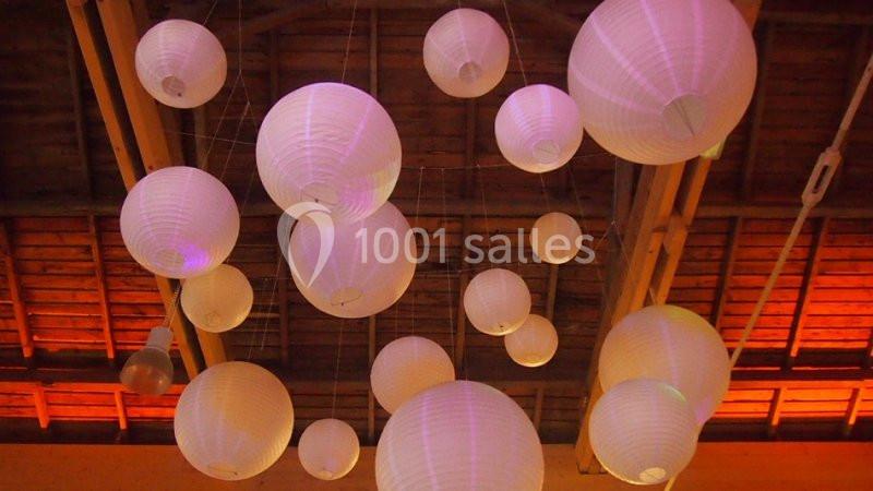 Lampions en papier blanc suspendus au plafond d'une structure en bois, éclairés par une lumière tamisée orange.