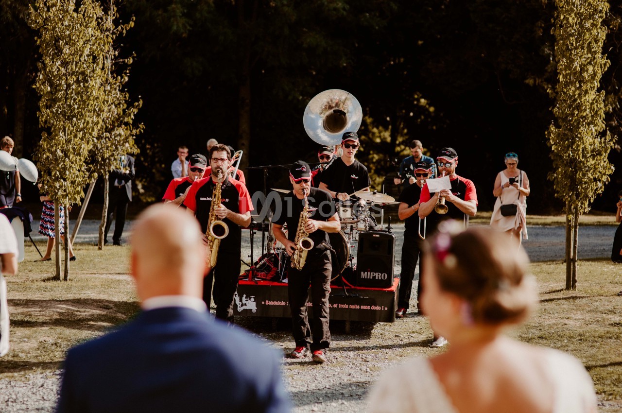 Un groupe de musiciens joue en plein air lors d'un événement, entouré d'arbres et de spectateurs.