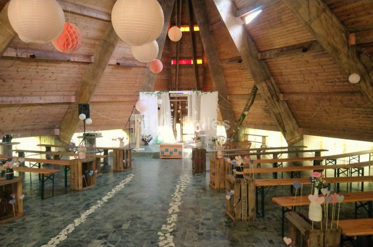 Intérieur d'une salle en bois avec bancs, décorations suspendues et allée centrale ornée de pétales blancs.