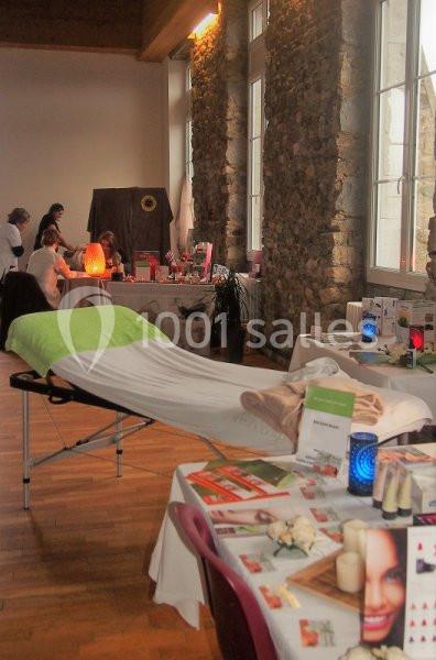 Table de massage avec drap vert dans une salle lumineuse, entourée de stands de bien-être et de décoration.