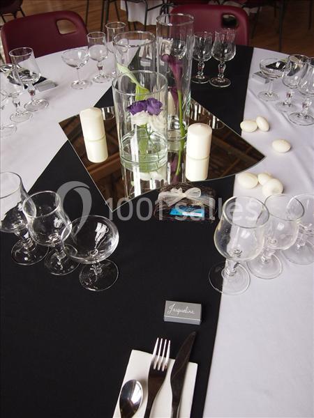 Table dressée avec nappes noires et blanches, verres, couverts, bougies, miroirs et vase contenant une fleur violette.