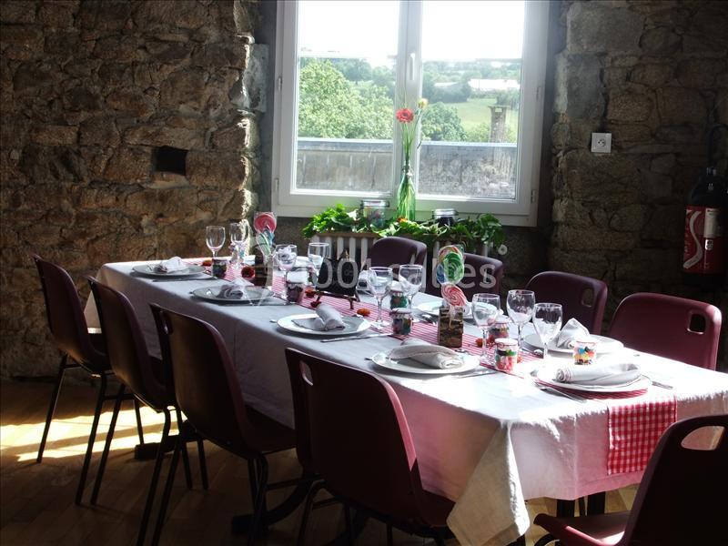 Table dressée avec nappes blanches et rouges, vaisselle et verres, dans une pièce en pierre avec vue sur la campagne.