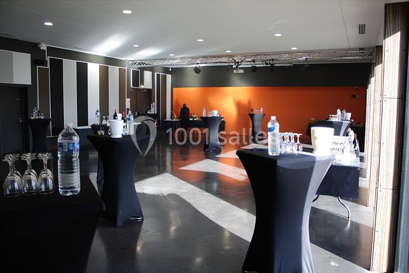 Salle de réception avec tables hautes noires, verres et bouteilles disposés pour un événement.