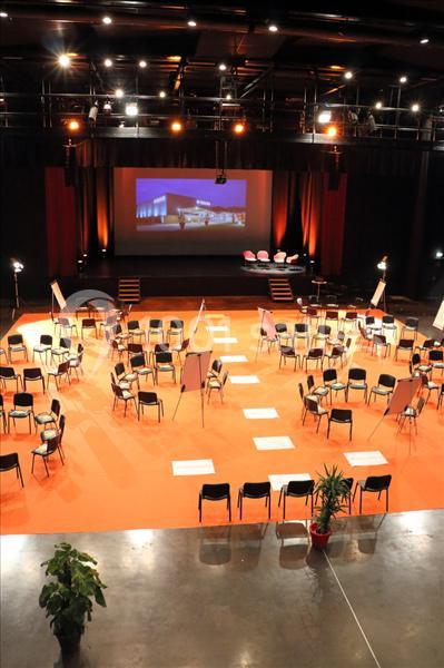 Salle de conférence aménagée avec des chaises disposées en cercle, écrans et projecteurs allumés.