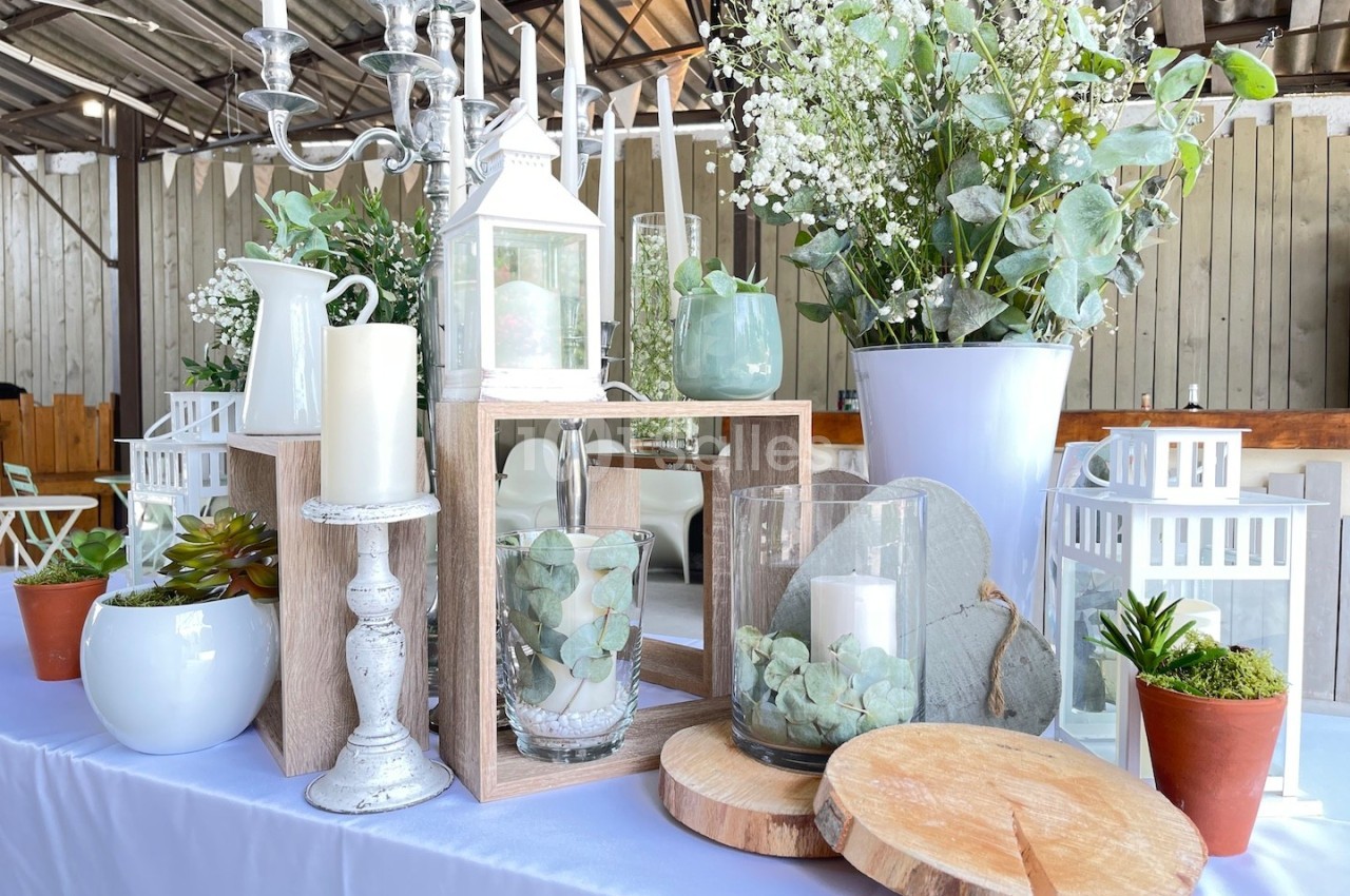 Décoration de table avec bougies, lanternes, plantes et fleurs dans un cadre lumineux et rustique.