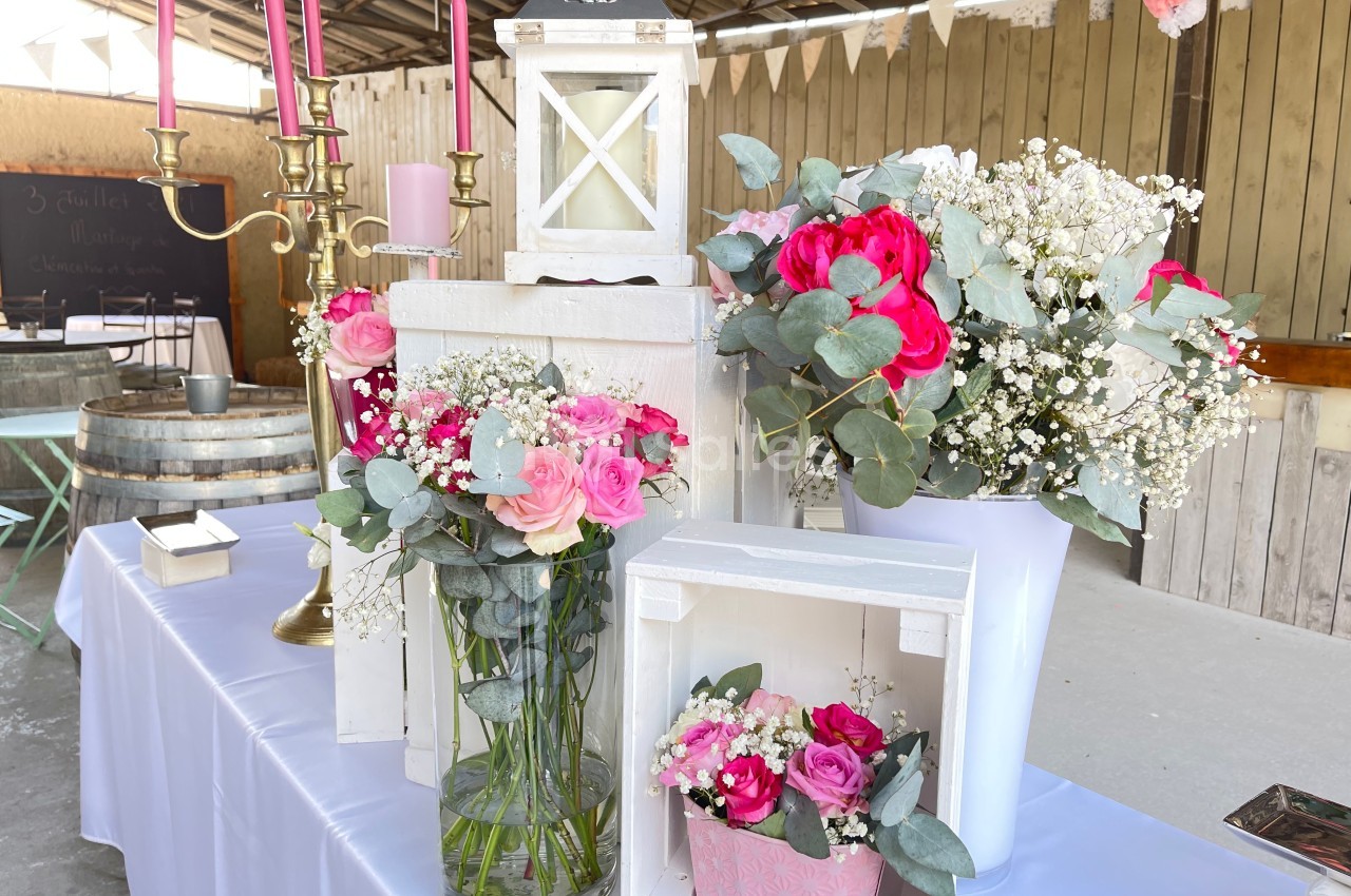 Décoration florale avec roses roses et rouges, gypsophiles et feuillage, disposée sur une table dans un cadre rustique.