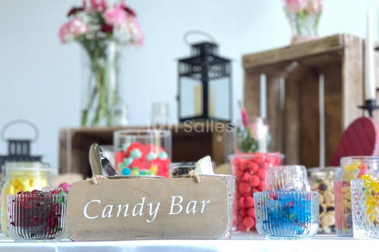 Buffet de bonbons colorés avec un panneau ’Candy Bar’, des bocaux en verre et une décoration florale en arrière-plan.