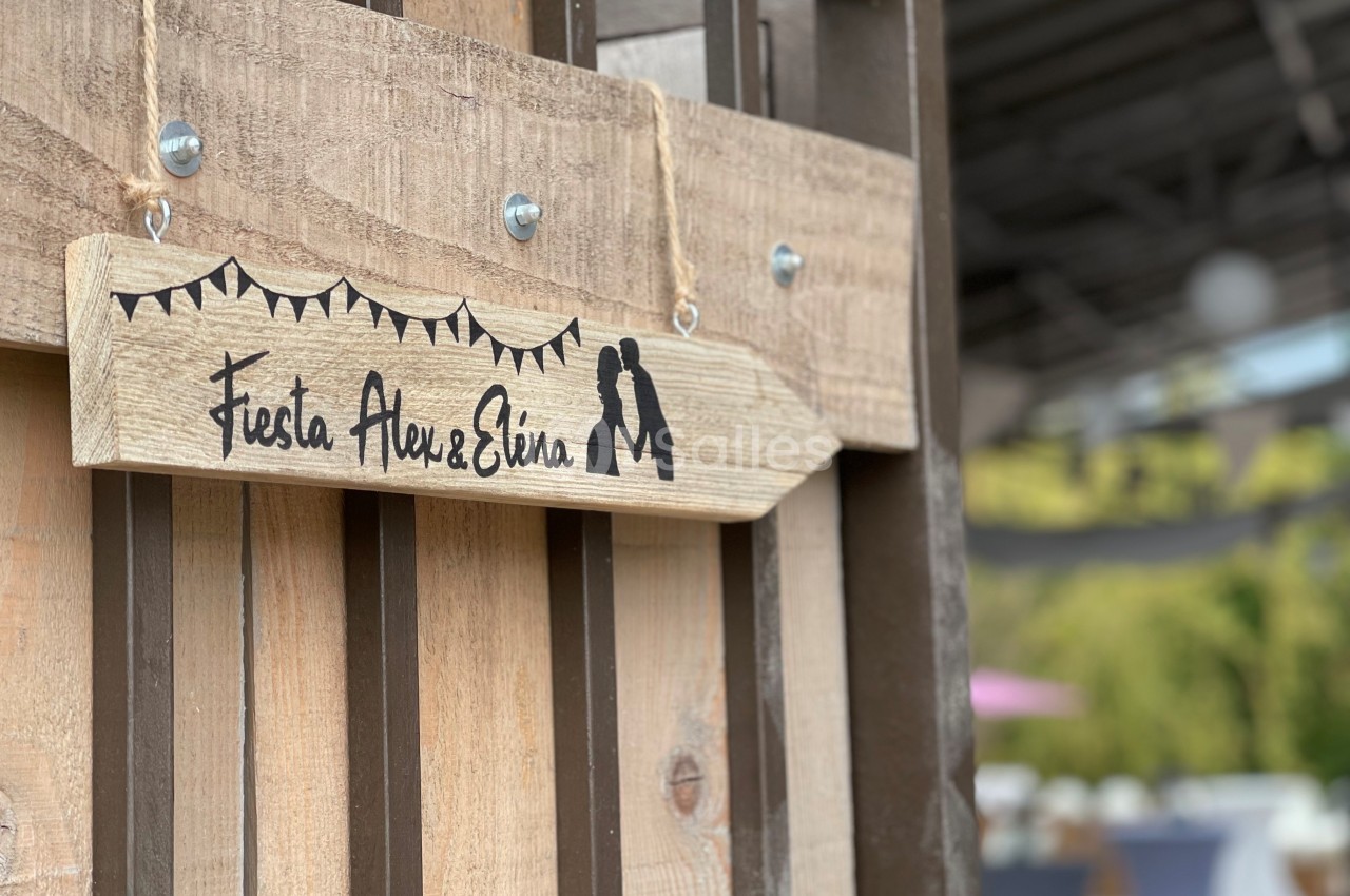 Pancarte en bois suspendue avec l'inscription ’Fiesta Alex & Elvia’ et des silhouettes décoratives, en extérieur.