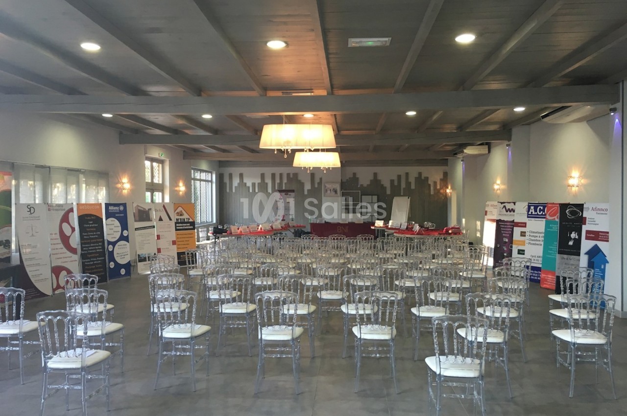 Salle de conférence aménagée avec des chaises transparentes et des stands promotionnels alignés au fond.