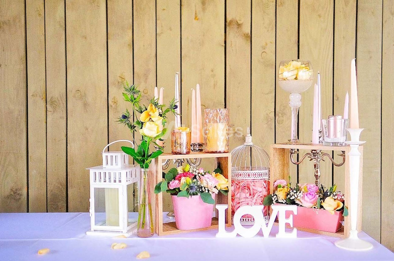 Décoration de table avec fleurs, bougies, lanternes et lettres formant le mot ’LOVE’ devant un fond en bois clair.