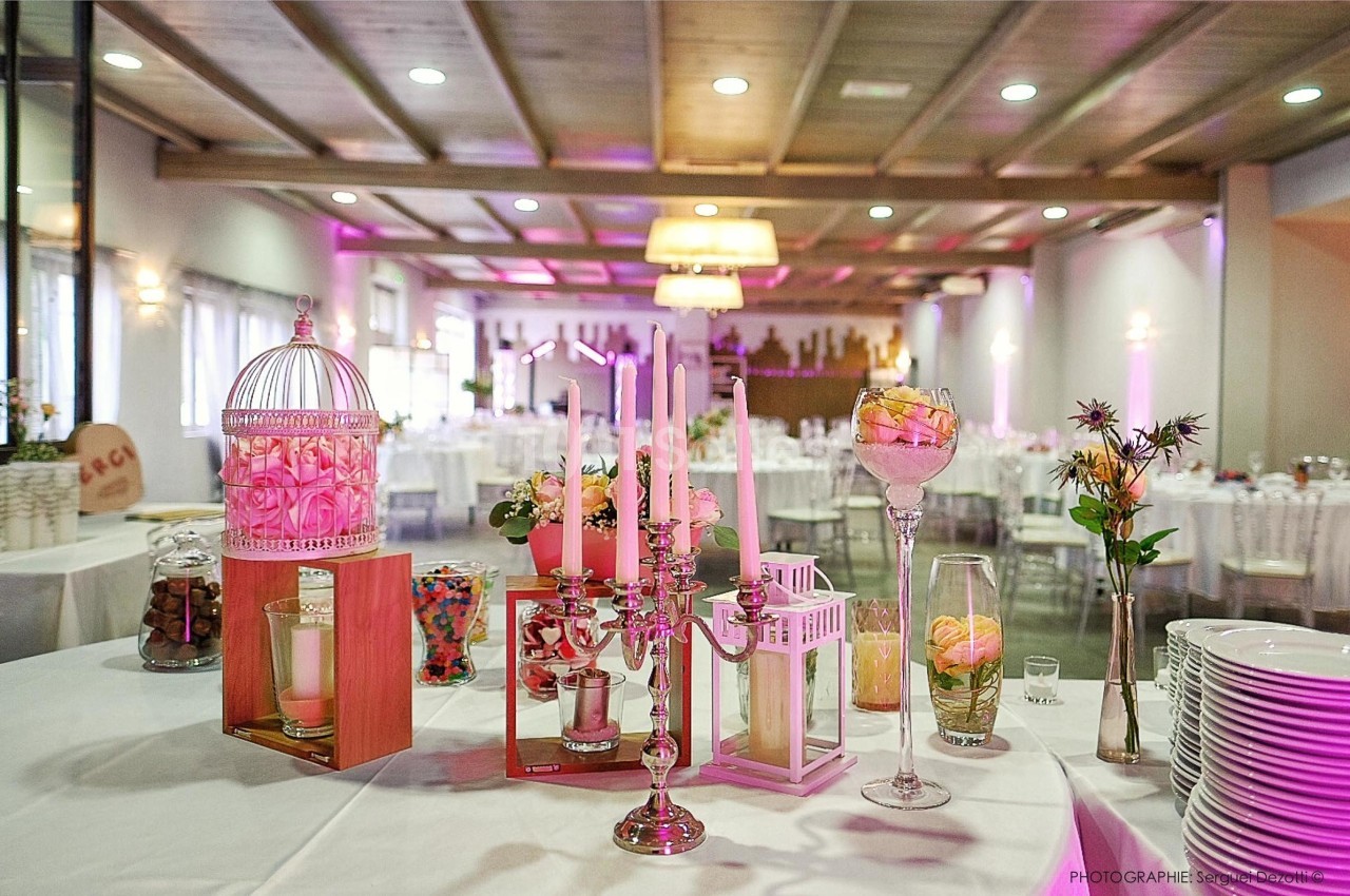 Décoration de table avec bougies, bonbonnières et fleurs dans une salle de réception lumineuse et élégante.