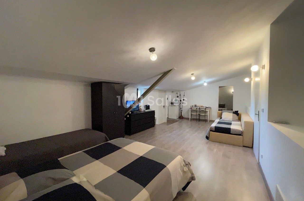 Chambre mansardée avec deux lits, un canapé, une table à manger et un éclairage suspendu, décor moderne et épuré.