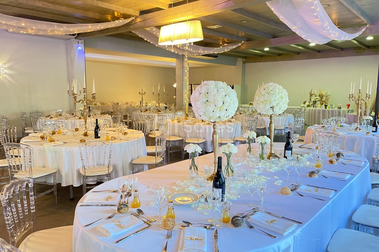 Salle de réception décorée pour un mariage, avec tables dressées, chandeliers, fleurs blanches et éclairage chaleureux.