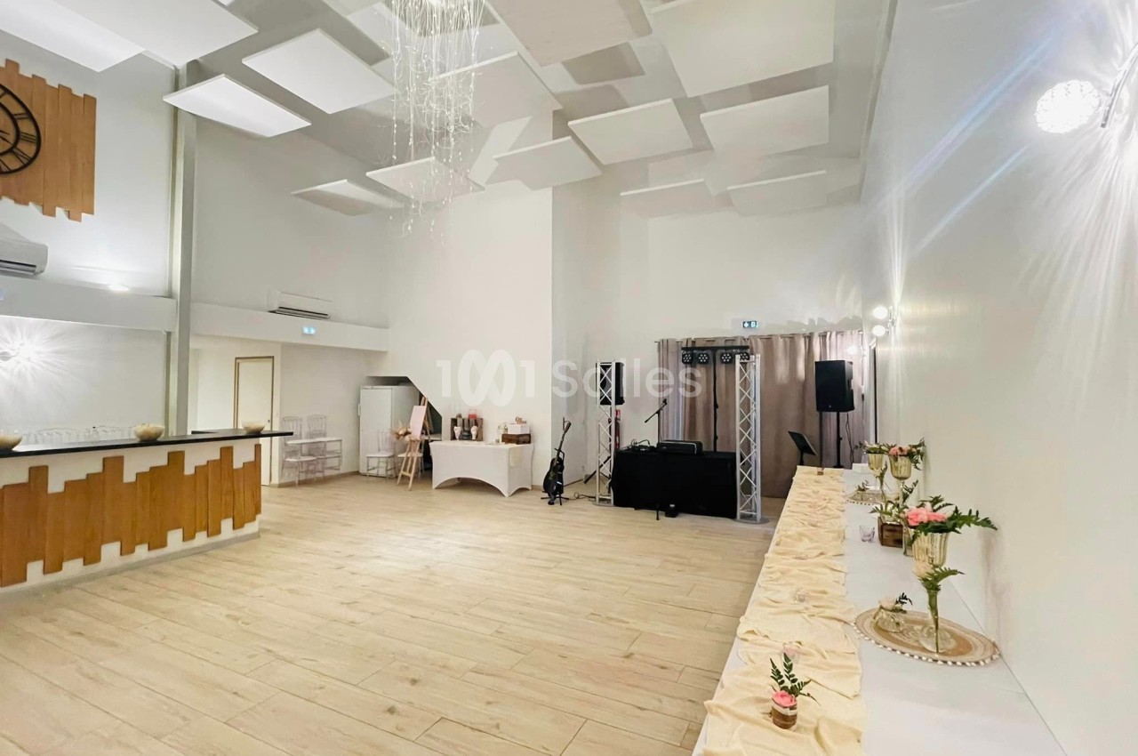Salle lumineuse avec parquet clair, bar en bois, table décorée et espace équipé pour un événement ou une réception.