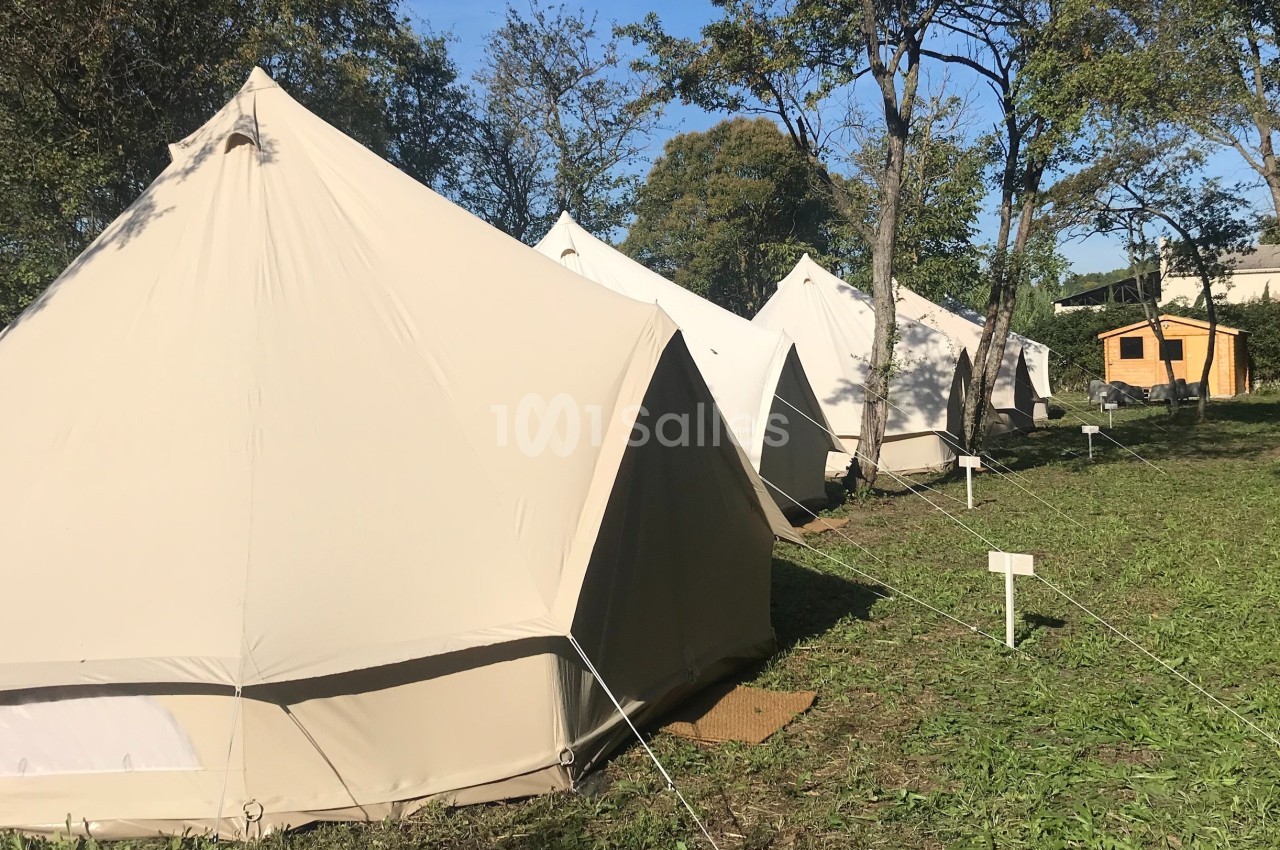 Tentes beige en toile installées en rangée sur une pelouse entourée d'arbres, par une journée ensoleillée.