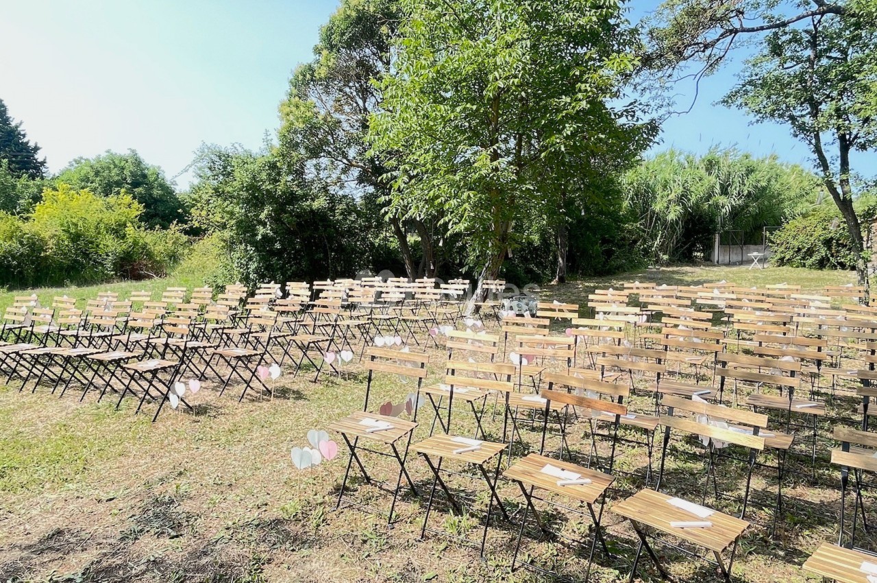 Chaises en bois disposées en rangées sur une pelouse, entourées d'arbres, dans un cadre extérieur ensoleillé.