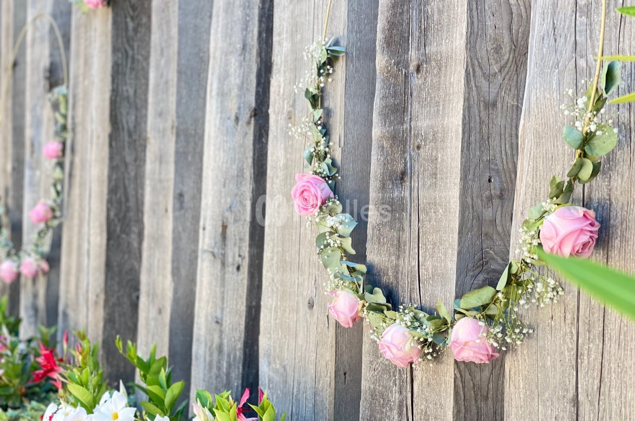 Guirlandes de fleurs roses suspendues sur une clôture en bois, avec des plantes colorées en bas.