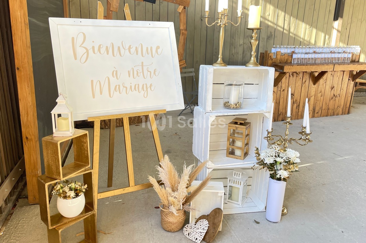 Décoration de mariage avec panneau de bienvenue, bougies, fleurs séchées et caisses en bois dans un espace extérieur.