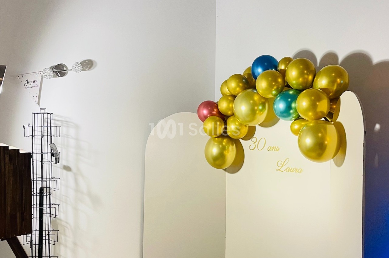 Mur décoratif avec des ballons dorés, roses et bleus formant une arche, et l'inscription ’30 ans Laura’.