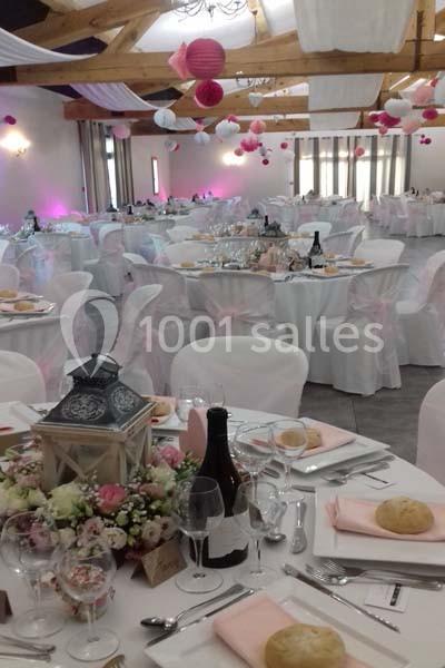 Salle de réception décorée pour un mariage, avec tables dressées, nappes blanches, fleurs et lanternes.