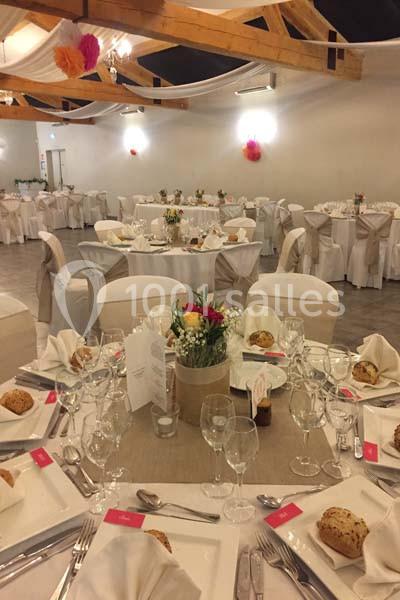 Salle de réception décorée avec des tables rondes dressées, nappes blanches et centres de table fleuris.