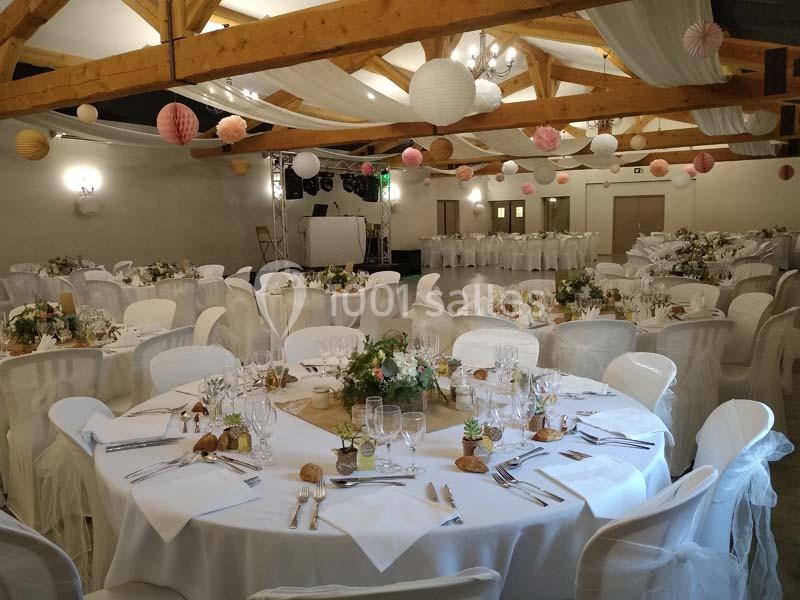 Salle de réception décorée avec des tables rondes dressées, des chaises blanches et des lanternes suspendues au plafond en…
