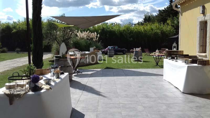 Terrasse extérieure aménagée avec tables, nappes blanches et décorations, entourée de verdure sous un ciel dégagé.