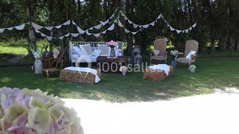 Décoration champêtre avec canapé, fauteuils, bottes de paille et guirlandes dans un jardin verdoyant.