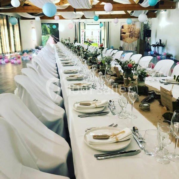 Grande table de réception décorée avec nappes blanches, vaisselle élégante et arrangements floraux, dans une salle festive.