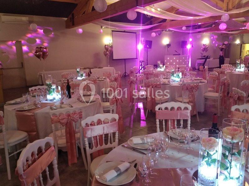 Salle de réception décorée dans des tons roses et blancs avec des tables dressées et des éclairages d'ambiance.