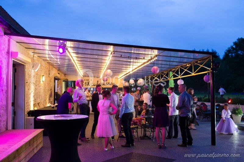 Groupe de personnes discutant et dansant sous une pergola éclairée en soirée, avec une ambiance festive.