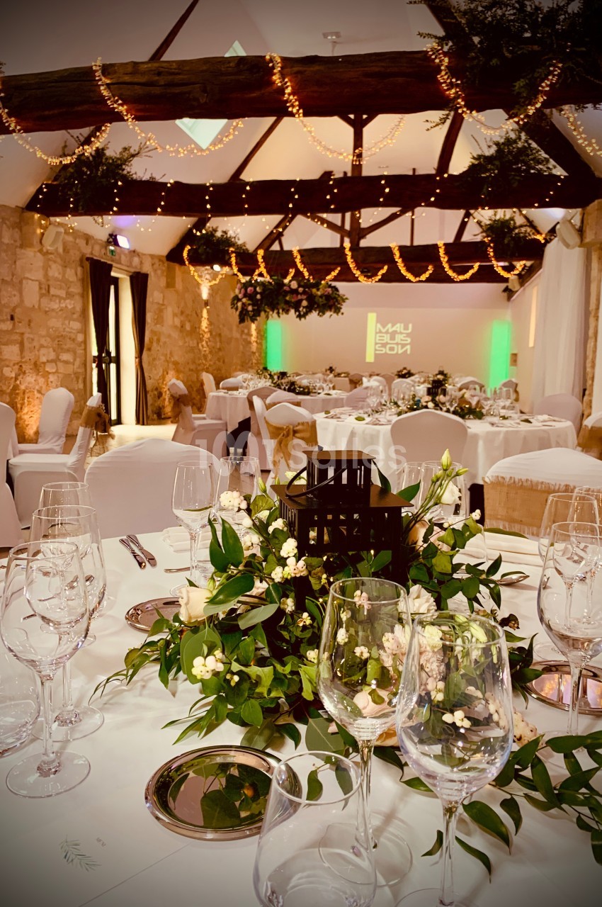 Salle de réception décorée avec des guirlandes lumineuses, des tables dressées et des compositions florales élégantes.