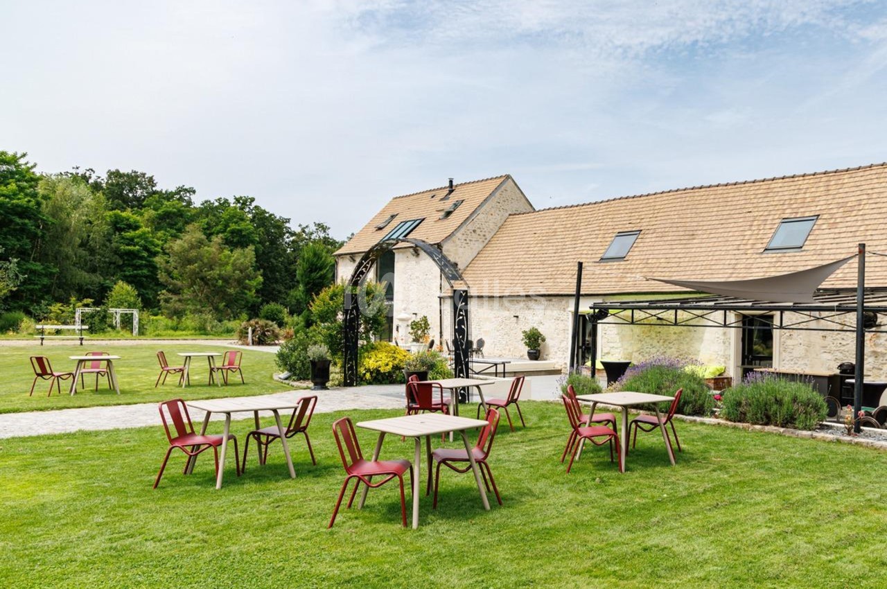 Tables et chaises disposées sur une pelouse devant un bâtiment en pierre avec toit en tuiles, par temps clair.