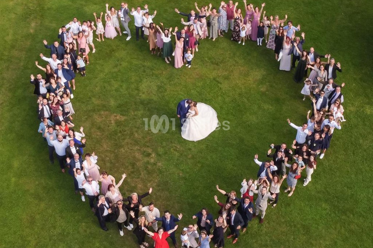 Vue aérienne d'un couple de mariés au centre d'un cœur formé par des invités sur une pelouse verte.
