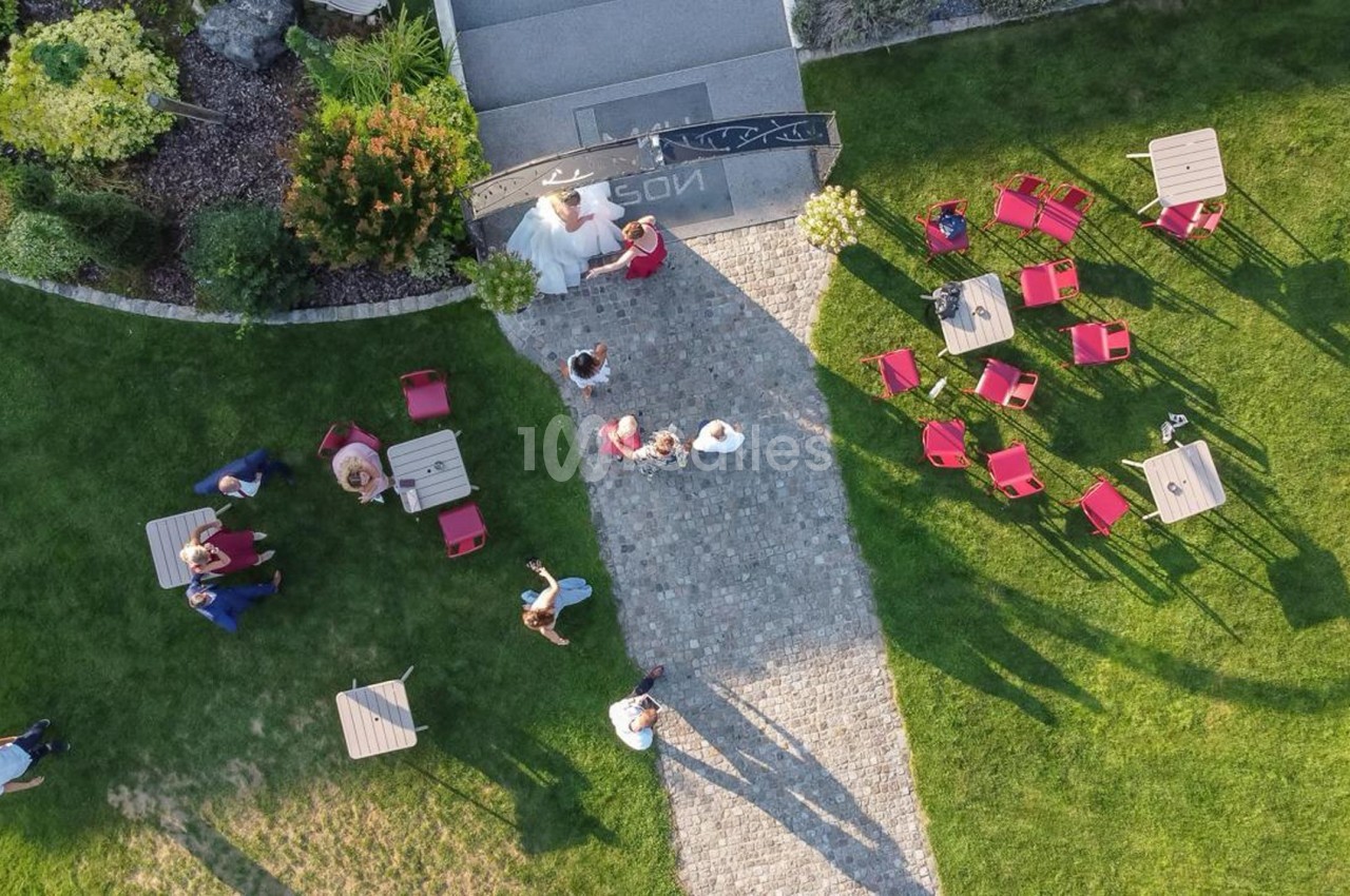 Vue aérienne d'un jardin avec des tables, des chaises rouges et des personnes rassemblées sur une allée pavée.