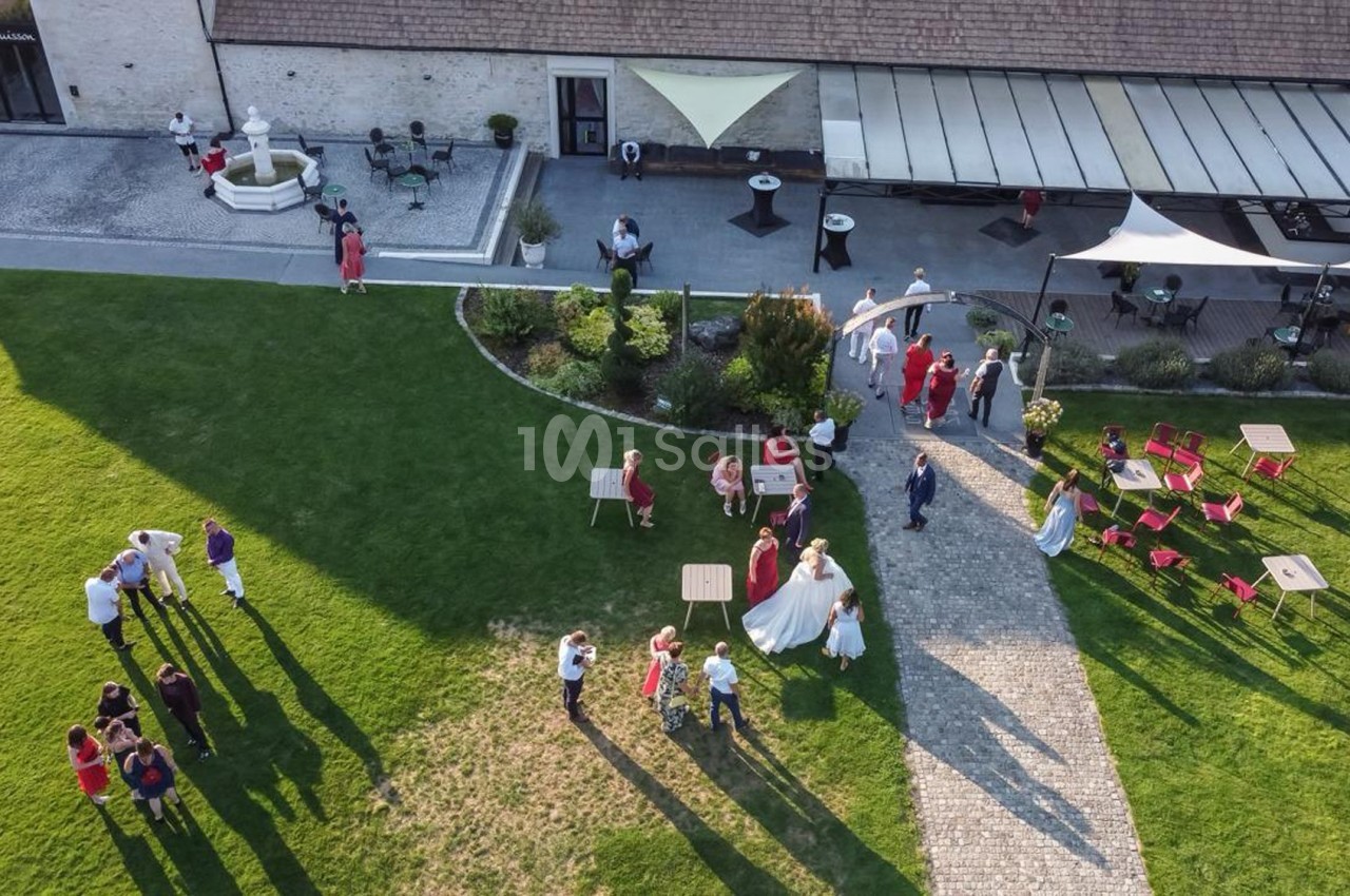 Vue aérienne d'un jardin avec des invités rassemblés lors d'une réception en plein air près d'un bâtiment.
