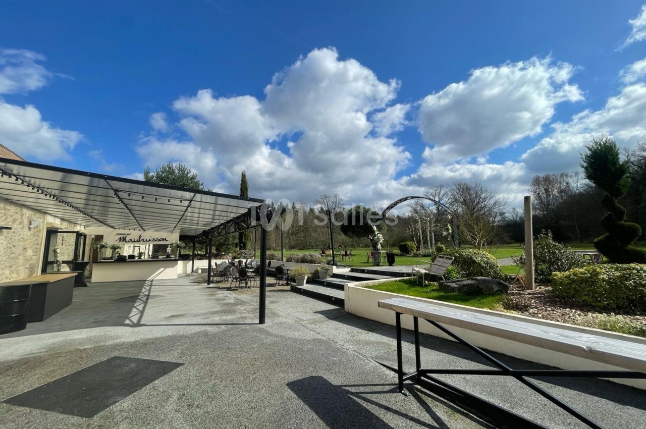 Terrasse aménagée avec pergola, mobilier extérieur et vue sur un jardin verdoyant sous un ciel partiellement nuageux.