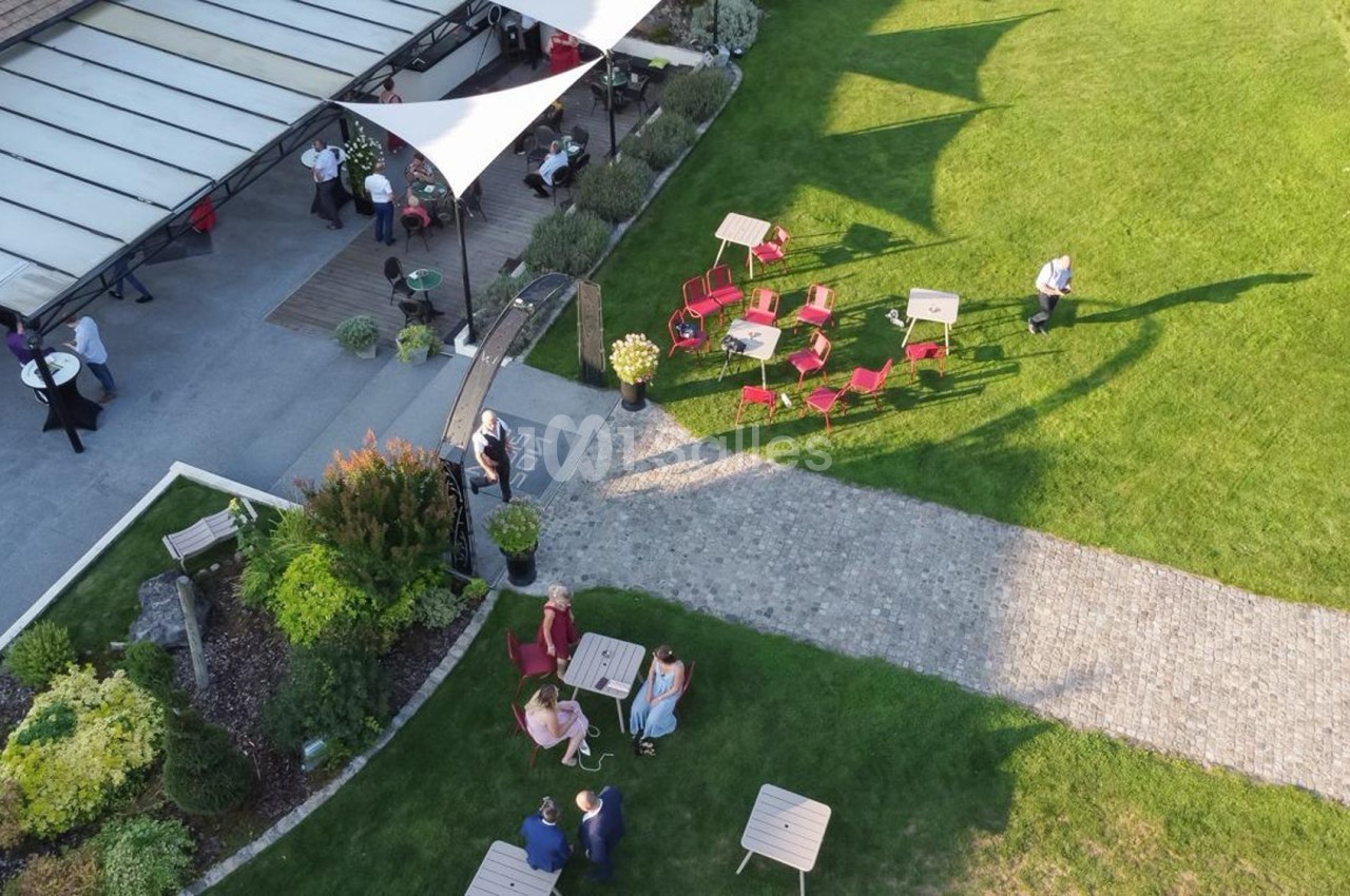 Vue aérienne d'un jardin avec des tables, des chaises rouges, des allées pavées et une terrasse couverte animée.