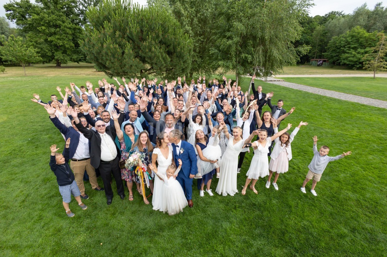 Groupe de personnes célébrant un mariage en plein air, souriants et levant les bras sur une pelouse verdoyante.
