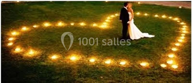Un couple en tenue de mariage se tient au centre d'un cœur formé par des bougies allumées sur une pelouse.