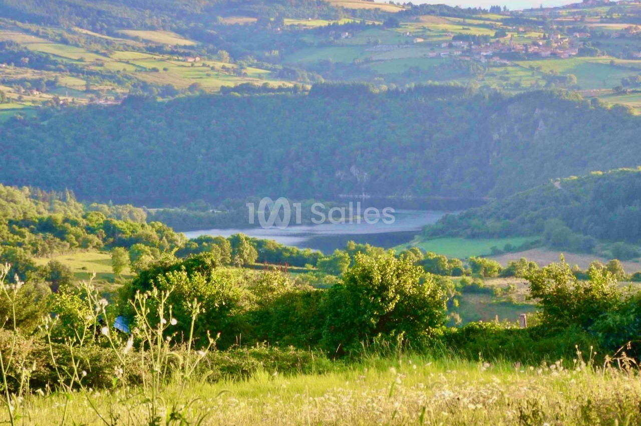 Paysage vallonné avec un lac entouré de forêts et de prairies verdoyantes sous une lumière douce.