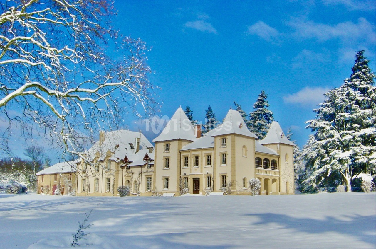 Manoir blanc entouré de neige, avec un ciel bleu clair et des arbres partiellement recouverts de neige.