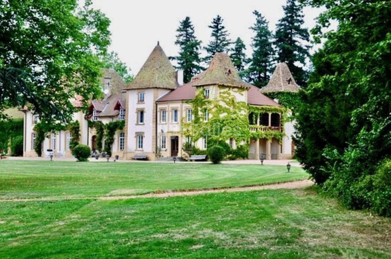 Manoir entouré de pelouses verdoyantes, avec des toits en tuiles et des arbres en arrière-plan.