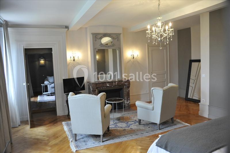 Salon élégant avec cheminée en marbre, deux fauteuils, un miroir, un lustre et un parquet en bois clair.