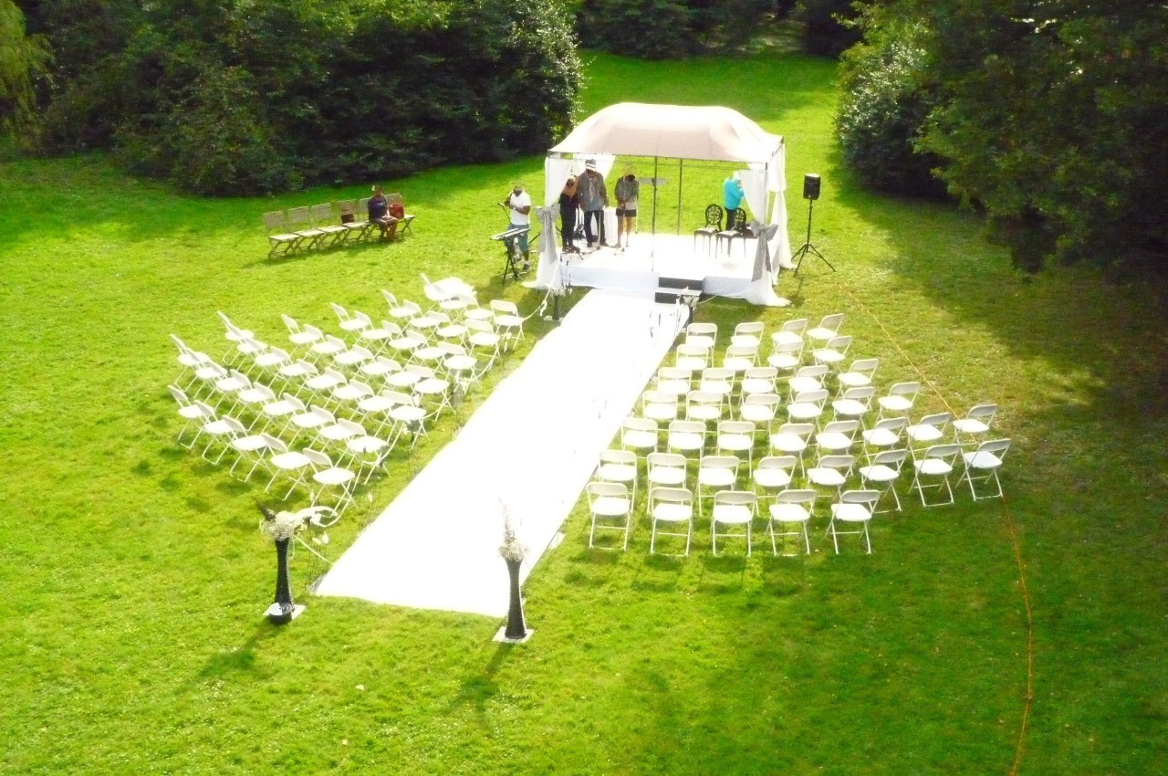 Disposition de chaises blanches en extérieur autour d'une allée menant à une petite scène sous une tente blanche.
