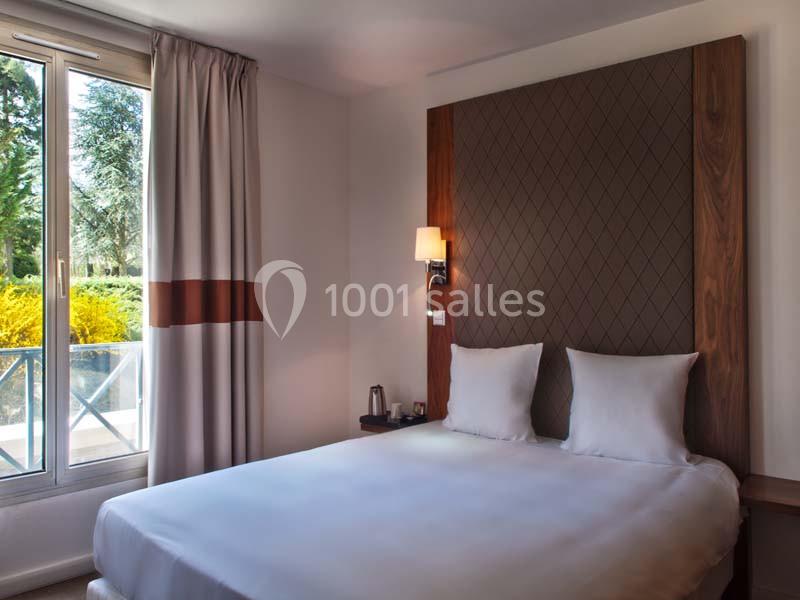 Chambre lumineuse avec un lit double, une grande fenêtre donnant sur un jardin et une décoration sobre.