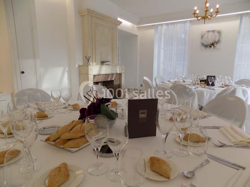 Table élégamment dressée avec nappes blanches, verres, couverts, pains et décoration florale dans une salle lumineuse.