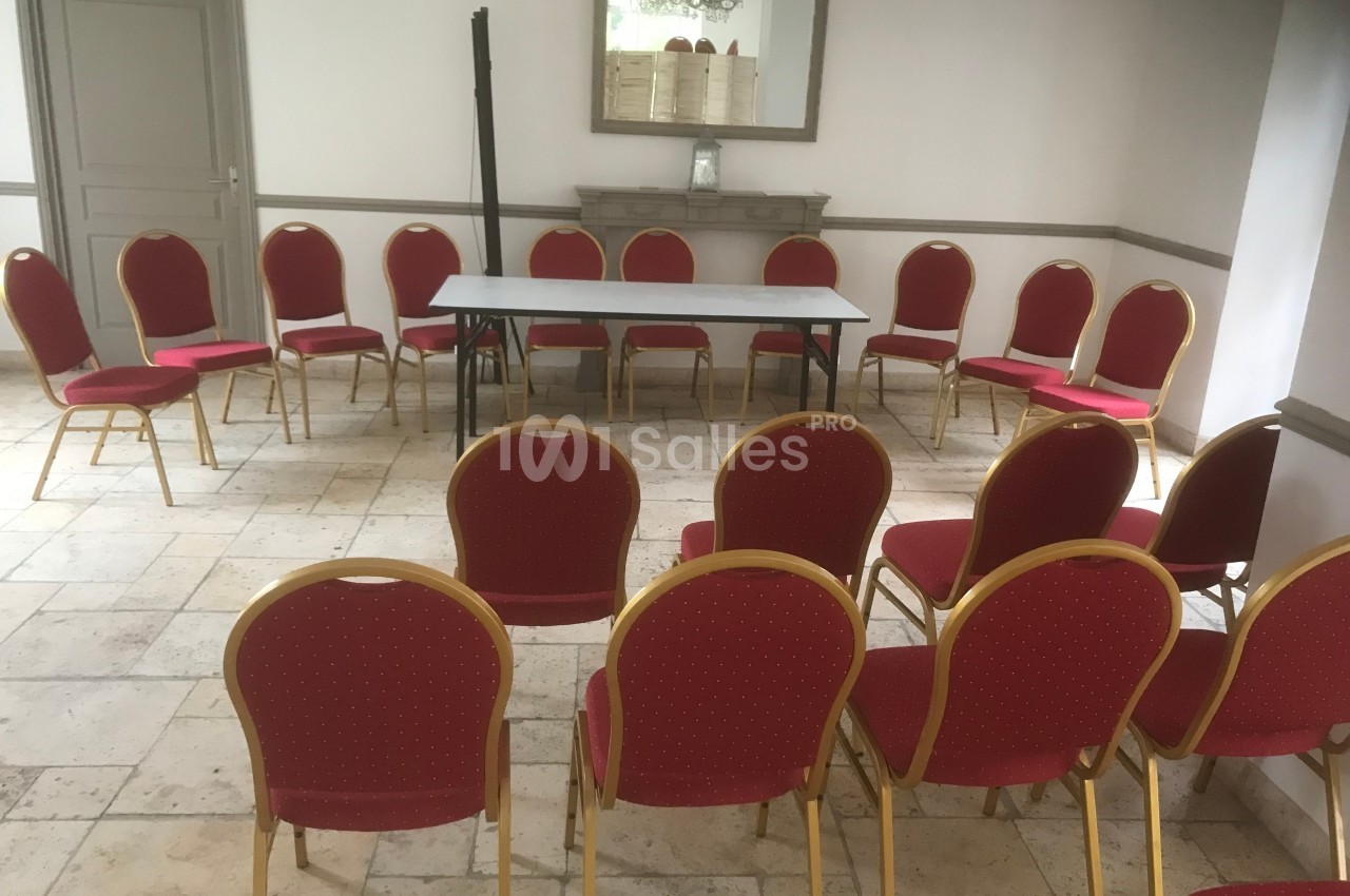 Chaises rouges disposées en cercle autour d'une table rectangulaire dans une salle lumineuse au sol carrelé.